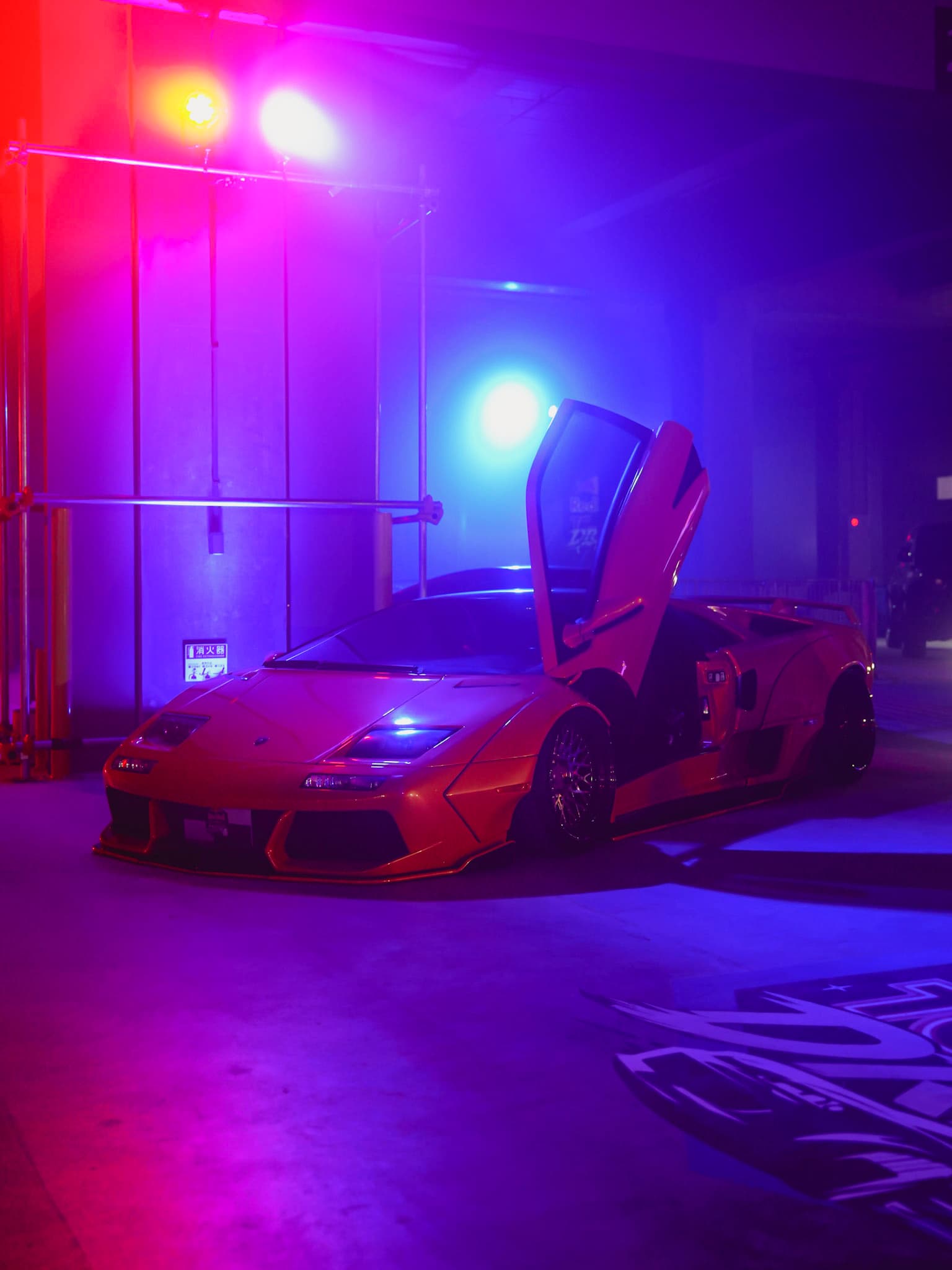 Orange Lamborghini with a scissor door raised under purple and blue show lighting