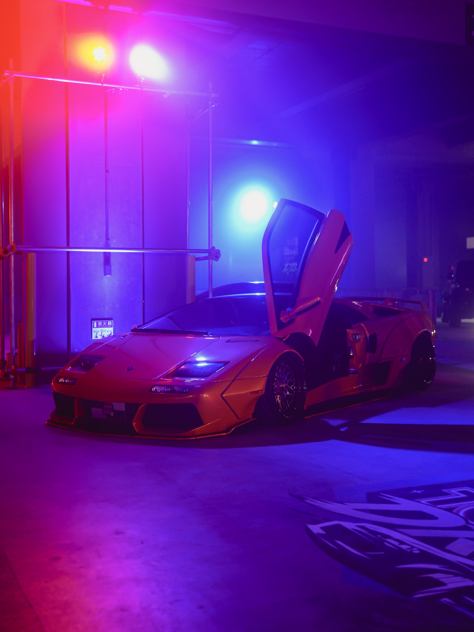 Orange Lamborghini with a scissor door raised under purple and blue show lighting